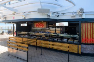Buffetbereich eines Grillrestaurants mit verschiedenen Gerichten und Stehtischen im Freien, mit Blick auf das Meer.