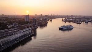 Luftaufnahme eines Hafens bei Sonnenuntergang mit einem Schiff auf dem Wasser und der Stadtlandschaft im Hintergrund.irit Hamburg